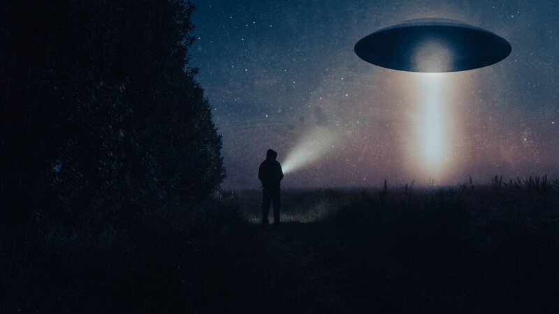 Ein Science-Fiction-Konzept eines Mannes mit einer Taschenlampe, der ein außerirdisches UFO betrachtet. Schwebend über einem Feld in einer gespenstischen, nebligen Nacht auf dem Lande. – Bild: Not Released (NR)/​David Wall