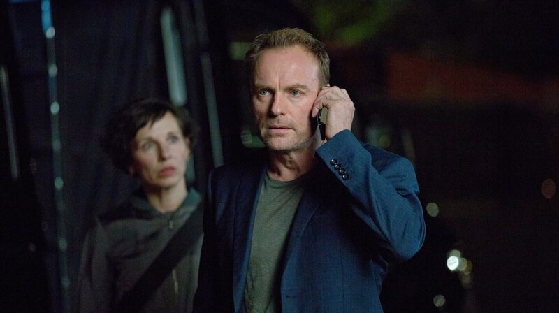 Ein belebter Platz mitten in der Stadt, 12 Uhr mittags. Gerade winkt die Studentin Mina Jiang (Yun Huang) noch ihrer Kommilitonin Luise (Paula Kroh) von weitem zu, als sie plötzlich tot zusammenbricht. Ein Schuss in den Hinterkopf führt die Kommissare Rubin (Meret Becker) und Karow (Mark Waschke) in die historische Mitte Berlins. – Karow (Mark Waschke) und Rubin (Meret Becker) versuchen das Geschehen in der Villa des Colloquiums zu belauschen. – Bild: rbb/​die film gmbh/​Volker Roloff