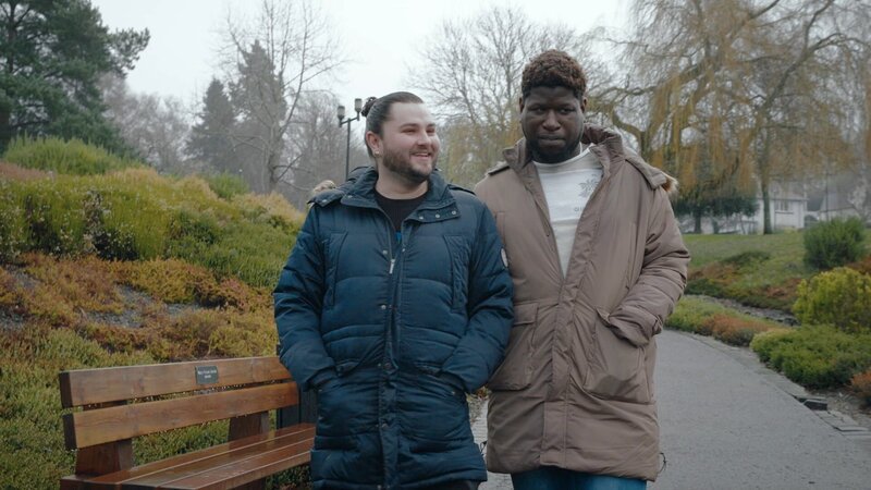 L-R: Calum und Marvin gehen zusammen in einem Park in Großbritannien spazieren und sprechen über ihre Liebe. – Bild: 2022 Warner Bros. Discovery, Inc. or its subsidiaries and affiliates. All rights reserved.