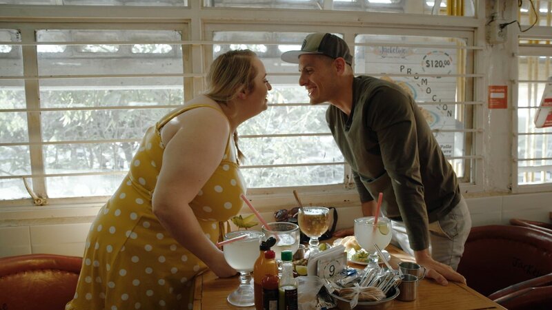 Kadie und Alejandro stehen über einen Tisch gelehnt und küssen sich in einem Marktrestaurant in Mexiko. – Bild: Warner Bros. Discovery