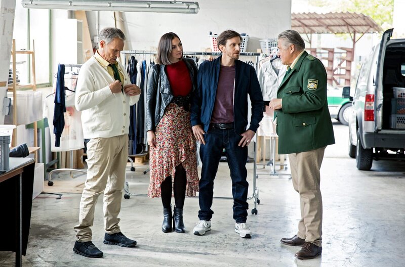 Hubert (Christian Tramitz, l.) und Girwidz (Michael Brandner, r.) verdächtigen Sven Lüttges (Vivian Frey, 2.v.r.), zusammen mit seiner Frau (Komparsin), Klamotten aus der Altkleiderverwertung entwendet zu haben, um sie hochpreisig zu verkaufen. – Bild: ARD/​Kai Neunert