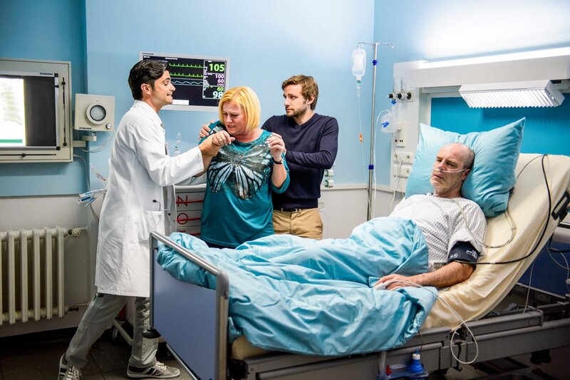 Dr. Behring (Maximilian Grill, l.), Erika Heller (Petra Kleinert, 2.v.l.), Martin Heller (Jonas Minthe, 2.v.r.) und Clemens Heller (Peter Kremer, r.) streiten sich am Krankenbett. – Bild: ORF/​ZDF/​Willi Weber