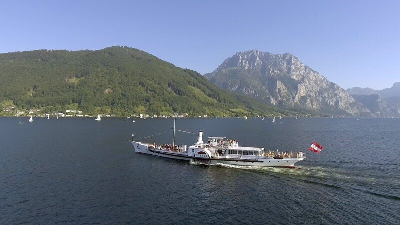 „Sommerfrische – Reisen wie zu Kaisers Zeiten“, Das Vielvölkerreich der Habsburger stellte einen kulturell wie gesellschaftlich einzigartigen Kosmos dar. Die nostalgische Verklärung dieser Ära begann noch vor dem Ende des Habsburgerreichs und hält bis heute an, vor allem in Orten, die mit einer der schönsten Errungenschaften der Donaumonarchie verbunden sind – der Sommerfrische. Das vornehmlich adelige und großbürgerliche Sommervergnügen, dessen Wurzeln in der Biedermeierzeit liegen und dem – wenn auch in bescheidenerem Rahmen – bis in die Zwischenkriegszeit gefrönt wurde, wird in dieser Dokumentation in all seinen Facetten gezeigt: von den populärsten Reiseziele vergangener Tage über die spezielle Reisekultur bis zu Transportmitteln und -wegen.Das „Fin de sičcle“ wurde zum Höhepunkt der Sommerfrische. Man reiste mit den Annehmlichkeiten der Stadt aufs Land, um dort wie in einem Freiluftsalon die Vorzüge von gut gepflegter Natur und urbaner Geselligkeit miteinander zu verbinden. Man schwärmte von Triest, von der Riva in Pola und vom milden Klima Abbazias. Damals entdeckte man den Lago di Garda, den Wörthersee und eroberte die Gipfel der Alpen. Das Reisen im alten Österreich war untrennbar mit der verkehrstechnischen Erschließung des Großreichs verbunden. Das Salzkammergut gilt als Wiege der Sommerfrische. Der Kurbetrieb am Traunsee war zutiefst verbunden mit dem österreichischen Kaiserhaus und der Nähe zu Ischl, wo Kaiser Franz Joseph seine Sommer verbrachte. Bis heute konnten Orte wie Gmunden viel vom Flair vergangener Tage bewahren. Während am Traunsee überwiegend Mitglieder der nationalen und internationalen Aristokratie dominierten, wurde das restliche Salzkammergut bald durch das gehobene Bürgertum erschlossen. Mitte des neunzehnten Jahrhunderts entdeckte man den Attersee und die ersten Sommervillen der Bourgeoisie entstanden. Fasziniert vom Türkisblau des Wassers am Attersee mischten sich Fotografen, Maler, Komponisten und Dichter – von Gustav Mahler bis Gustav Klimt -unter das reiche Großbürgertum. In der 1890 erbauten Villa Langer in Steinbach am Attersee wird die Sommerfrische wiederbelebt, wie sie Adelige, Großbürger und berühmte Künstler genossen haben.Wenn Komponisten Urlaub machten, suchten sie meist nach Inspiration und Ruhe. Als kreative Refugien dienten ihnen gerne Seebäder, Komponier-Häuschen oder ein abgelegenes Waldhaus. Gerne bedienten sie dabei das Klischee des genialen Eremiten, auch wenn so mancher von ihnen den Freuden des Lebens nicht abgeneigt war. Johannes Brahms war einer jener Komponisten, die ihre produktivsten Zeiten während ihres Urlaubs hatten. Sommerfrische war für ihn niemals nur Amüsement. Einige seiner berühmtesten Werke komponierte er in Pörtschach am Wörthersee. Mit dem Anschluss der Bahnstrecke Wien-Klagenfurt an die „k.u.k. Südbahn“ wurde der Aufenthalt am Wörthersee zu einer gut erreichbaren Attraktion und Pörtschach zu einem der edelsten Sommerfrische-Orte in der Donau-Monarchie. Die Sommerfrische – der Historiker Hanns Haas nennt sie eine „verlorene touristische Kulturform“ – war keine „Verabredung mit dem Fremden“, sondern bot Kontinuität und bezog ihren Reiz aus der Wiederkehr des Vertrauten. Wo früher mondänes Leben und zeitgemäßer Chic dominierten, begegnet uns heute mitunter nur noch milde Patina. Aber es gibt sie noch, die Orte und Landschaften, wo trotz zeitgemäßer Technik versucht wird, das Flair vergangener Tage zu erhalten. Dieses Flair gilt es zu erspüren und zu ergründen, um den Mythos der Sommerfrische erfahrbar zu machen.Eine Dokumentation von Björn Kölz und Gernot StadlerIm Bild: SENDUNG: ORF2 – SO – 12.07.2020–09:05 UHR. – Veroeffentlichung fuer Pressezwecke honorarfrei ausschliesslich im Zusammenhang mit oben genannter Sendung oder Veranstaltung des ORF bei Urhebernennung. – Bild: ORF/Gernot Stadler „Sommerfrische – Reisen wie zu Kaisers Zeiten“, Das Vielvölkerreich der Habsburger stellte einen kulturell wie gesellschaftlich einzigartigen Kosmos dar. Die nostalgische Verklärung dieser Ära begann noch vor dem Ende des Habsburgerreichs und hält bis heute an, vor allem in Orten, die mit einer der schönsten Errungenschaften der Donaumonarchie verbunden sind – der Sommerfrische. Das vornehmlich adelige und großbürgerliche Sommervergnügen, dessen Wurzeln in der Biedermeierzeit liegen und dem – wenn auch in bescheidenerem Rahmen – bis in die Zwischenkriegszeit gefrönt wurde, wird in dieser Dokumentation in all seinen Facetten gezeigt: von den populärsten Reiseziele vergangener Tage über die spezielle Reisekultur bis zu Transportmitteln und -wegen.Das „Fin de sičcle“ wurde zum Höhepunkt der Sommerfrische. Man reiste mit den Annehmlichkeiten der Stadt aufs Land, um dort wie in einem Freiluftsalon die Vorzüge von gut gepflegter Natur und urbaner Geselligkeit miteinander zu verbinden. Man schwärmte von Triest, von der Riva in Pola und vom milden Klima Abbazias. Damals entdeckte man den Lago di Garda, den Wörthersee und eroberte die Gipfel der Alpen. Das Reisen im alten Österreich war untrennbar mit der verkehrstechnischen Erschließung des Großreichs verbunden. Das Salzkammergut gilt als Wiege der Sommerfrische. Der Kurbetrieb am Traunsee war zutiefst verbunden mit dem österreichischen Kaiserhaus und der Nähe zu Ischl, wo Kaiser Franz Joseph seine Sommer verbrachte. Bis heute konnten Orte wie Gmunden viel vom Flair vergangener Tage bewahren. Während am Traunsee überwiegend Mitglieder der nationalen und internationalen Aristokratie dominierten, wurde das restliche Salzkammergut bald durch das gehobene Bürgertum erschlossen. Mitte des neunzehnten Jahrhunderts entdeckte man den Attersee und die ersten Sommervillen der Bourgeoisie entstanden. Fasziniert vom Türkisblau des Wassers am Attersee mischten sich Fotografen, Maler, Komponisten und Dichter – von Gustav Mahler bis Gustav Klimt -unter das reiche Großbürgertum. In der 1890 erbauten Villa Langer in Steinbach am Attersee wird die Sommerfrische wiederbelebt, wie sie Adelige, Großbürger und berühmte Künstler genossen haben.Wenn Komponisten Urlaub machten, suchten sie meist nach Inspiration und Ruhe. Als kreative Refugien dienten ihnen gerne Seebäder, Komponier-Häuschen oder ein abgelegenes Waldhaus. Gerne bedienten sie dabei das Klischee des genialen Eremiten, auch wenn so mancher von ihnen den Freuden des Lebens nicht abgeneigt war. Johannes Brahms war einer jener Komponisten, die ihre produktivsten Zeiten während ihres Urlaubs hatten. Sommerfrische war für ihn niemals nur Amüsement. Einige seiner berühmtesten Werke komponierte er in Pörtschach am Wörthersee. Mit dem Anschluss der Bahnstrecke Wien-Klagenfurt an die „k.u.k. Südbahn“ wurde der Aufenthalt am Wörthersee zu einer gut erreichbaren Attraktion und Pörtschach zu einem der edelsten Sommerfrische-Orte in der Donau-Monarchie. Die Sommerfrische – der Historiker Hanns Haas nennt sie eine „verlorene touristische Kulturform“ – war keine „Verabredung mit dem Fremden“, sondern bot Kontinuität und bezog ihren Reiz aus der Wiederkehr des Vertrauten. Wo früher mondänes Leben und zeitgemäßer Chic dominierten, begegnet uns heute mitunter nur noch milde Patina. Aber es gibt sie noch, die Orte und Landschaften, wo trotz zeitgemäßer Technik versucht wird, das Flair vergangener Tage zu erhalten. Dieses Flair gilt es zu erspüren und zu ergründen, um den Mythos der Sommerfrische erfahrbar zu machen.Eine Dokumentation von Björn Kölz und Gernot StadlerIm Bild: SENDUNG: ORF2 – SO – 12.07.2020–09:05 UHR. – Veroeffentlichung fuer Pressezwecke honorarfrei ausschliesslich im Zusammenhang mit oben genannter Sendung oder Veranstaltung des ORF bei Urhebernennung. – Bild: ORF/Gernot Stadler