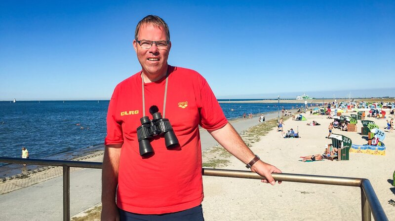 Camping am Meer! In Neuharlingersiel trennt nur der Deich den Campingplatz vom Strand. Da hat Rettungsschwimmer Dirk ordentlich zu tun. Kleine Schnittwunden durch Muscheln, Quallenstiche oder besetzte Strandkörbe – den Ostfriesen bringt so schnell nichts aus der Ruhe. – Bild: MDR/​timeline