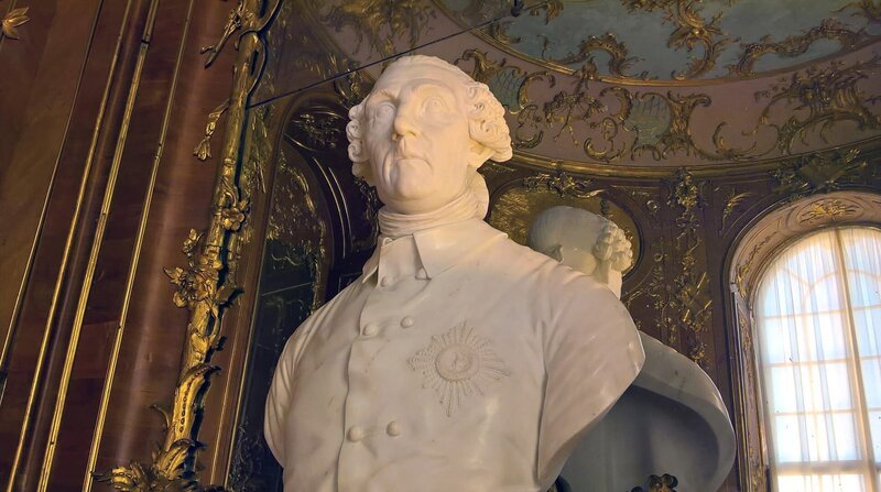 Schloss Sanssouci: Ein Ort – der Zeit scheinbar enthoben. Im Sommer, im Sonnenglanz, erstrahlt es in ganzer Pracht, Schönheit und Eleganz. Das kleine Lustschloss war schon im 18. Jahrhundert ein Publikumsmagnet und ist es bis heute. Auch, weil es wie kein anderer Platz verwoben ist mit der Geschichte seines Schöpfers – Friedrichs des Großen. – Büste von Friedrich dem Großen in der Bibliothek von Sanssouci – Bild: rbb / ZDF Schloss Sanssouci: Ein Ort – der Zeit scheinbar enthoben. Im Sommer, im Sonnenglanz, erstrahlt es in ganzer Pracht, Schönheit und Eleganz. Das kleine Lustschloss war schon im 18. Jahrhundert ein Publikumsmagnet und ist es bis heute. Auch, weil es wie kein anderer Platz verwoben ist mit der Geschichte seines Schöpfers – Friedrichs des Großen. – Büste von Friedrich dem Großen in der Bibliothek von Sanssouci – Bild: rbb / ZDF