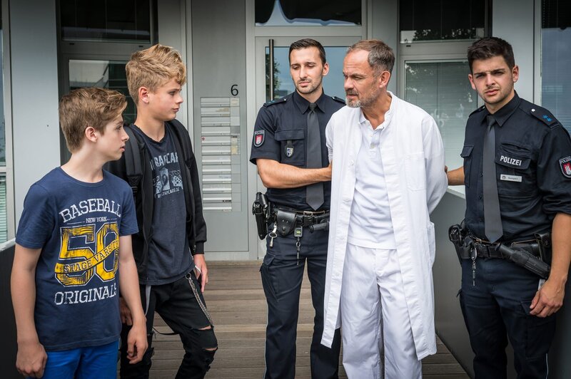 Noch immer wütend beobachten Till (Otto von Grevenmoor, 2. v. l.) und Marvin (Lewin Winter, li.), wie Dr. Götze (Matthias Leja, Mitte) abgeführt wird. Zu Recht! – Bild: NDR/​Boris Laewen