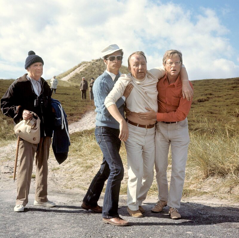 Zum Arzt geschleppt wird der übel zugerichtete Regierungsdirektor Warrlau (Ulrich Matschoss) von zwei jungen Männern (Burkhard Günther, Rolf Haaks, rechts). Kurgast Grimpe (Gustav Burmester, links) trägt sein Gepäck. – Bild: NDR/​Schweigmann