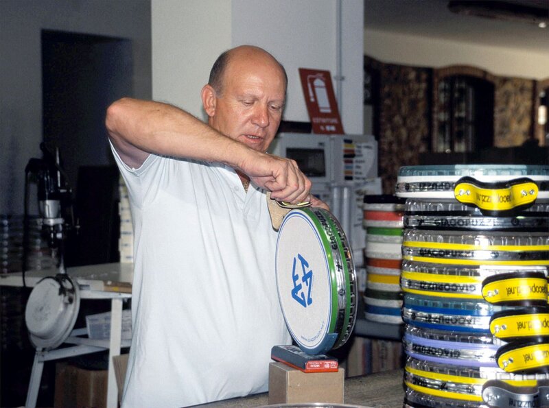 SWR SPIELE DER WELT, Tamburello in Italien, am Mittwoch um 13:30 Uhr im Südwestfernsehen. Tamburellohersteller mit Turm von Schlägern vor sich: Hier werden Tamburelloschläger hergestellt, in einem reinen Familienbetrieb, in dem Vater, Mutter und die drei Töchter all ihren Ehrgeiz in die perfekte Bespannung legen. – Bild: SWR