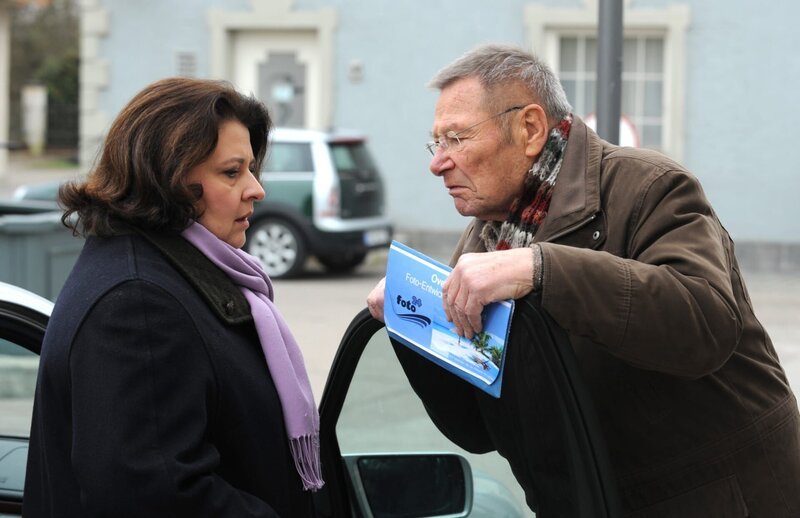 Alois bringt Monika ihre Fotos, die schon seit Tagen bei ihm zur Abholung bereit liegen. Von links: Monika Vogl (Christine Reimer) und Alois Preissinger (Erich Hallhuber sen.). – Bild: BR/​Marco Orlando Pichler