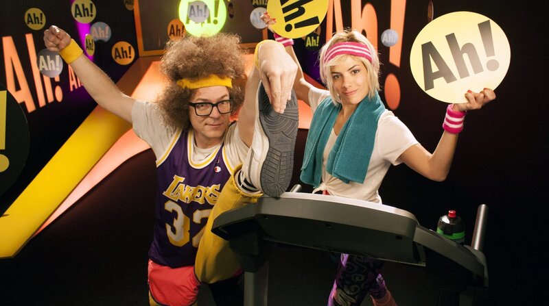 Heute wird es sportlich im Ah!-Studio! Also raus aus dem Fernsehsessel und mitgemacht, während die beiden Coaches Clarissa und Ralph ihr Fitnessprogramm präsentieren! Dabei klären sie ein für alle Mal, ob Pferde Warm-, Kalt- oder Vollblüter sind und dass das richtige Atmen bei jeder körperlichen Betätigung das A und O ist. – Bild: BR/​WDR/​Thorsten Schneider