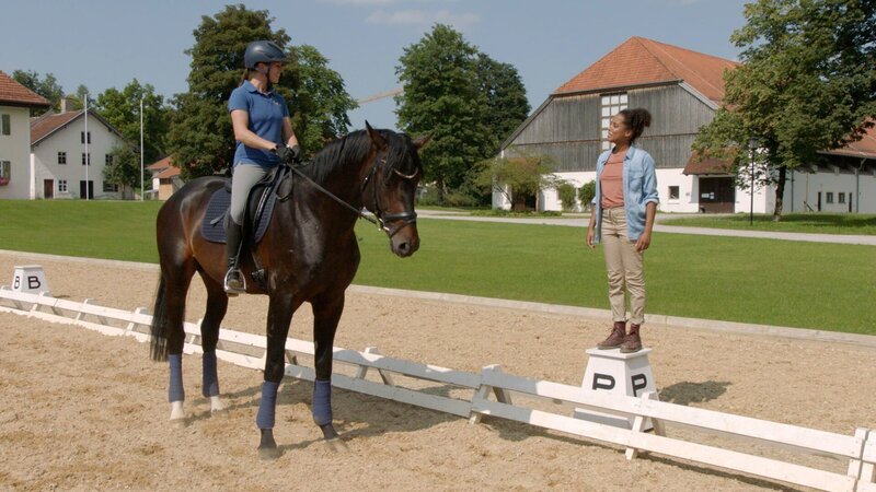 Auf dem großen Reitplatz trifft Pia (rechts) Bereiterin Michaela, die gerade den jungen Hengst Scalatore trainiert. – Bild: Das Erste