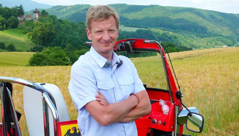 Für seine neue Expedition geht Michael Kessler buchstäblich an die Grenze. Rund 1.400 Kilometer legt der Comedian im Tuk Tuk zurück. Mit dem ostasiatischen Dreirad fährt er von Bayern bis an die Ostsee, immer entlang des ehemaligen deutsch-deutschen Grenzstreifens, um zu erfahren, ob 25 Jahre nach dem Mauerfall auch wirklich zusammen gewachsen ist, was zusammengehört. Der erste Teil der Expedition führt ihn vom alten Grenzstein im Dreiländereck nahe Hof zwischen Bayern, Sachsen und Tschechien bis nach Bad Sachsa im Harz. – Michael Kessler mit dem Tuk Tuk im Eichsfeld. – Bild: rbb/​Stefan Wieduwilt