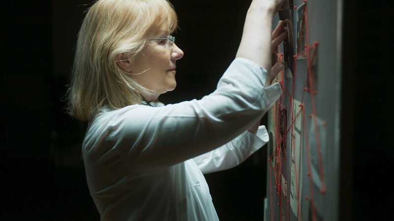 Die Gennat-Biografin Regina Stürickow vor einem Organigramm von Mordfällen aus den 1920ern. – Bild: ZDF und Arsenij Gusev.