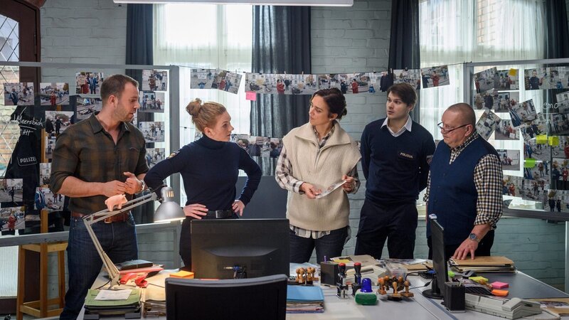 Die Ermittelnden Lars Pöhlmann (Dominic Boeer, l.), Paula Moorkamp (Stella Hinrichs, 2.v.l.), Karoline Joost (Nike Fuhrmann, M.), Eddi Jansons (Gustavs Gailus, 2.v.r.) und Jan Reuter (Udo Kroschwald, r.) diskutieren am Tisch von Eddi über die verschiedenen Tatverdächtigen im Revier. Könnte es eines der Vereinsmitglieder gewesen sein? Paula findet jedoch einen wichtigen Hinweis, der eine Person von außerhalb ins Visier nimmt. – Bild: ZDF