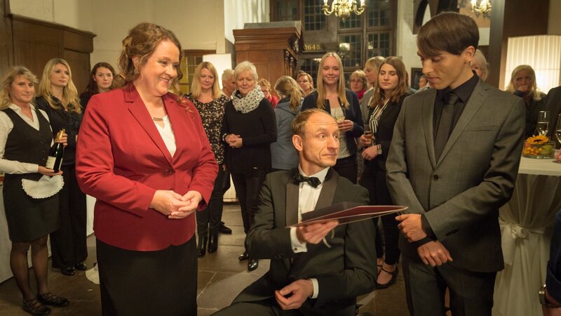 Der stark übergewichtige Franzose ist in Wismar aufgefallen. Am Abend vor seinem Tod hat im Rathaus eine Ehrung zugunsten des Mäzens Friedemann Romberg stattgefunden. Dort ist der Dicke ausgerechnet mit Hauptkommissar Jan Reuter zusammengestoßen (v.l.n.r. vorne: Susanna Sandvoss, Michael Schenk, Christian Wagner). – Bild: ZDF/​Marc Meyerbröcker