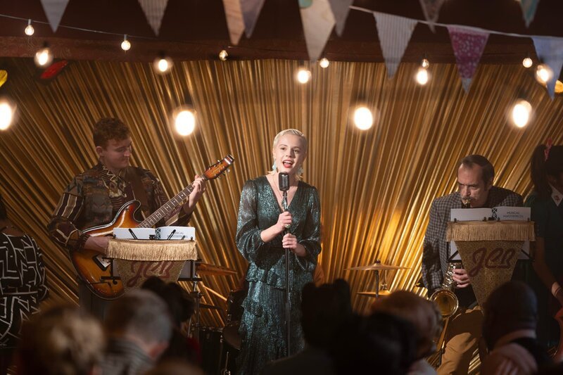Noch läuft das Gemeindefest perfekt. Die Band – mit Finn (Conor Cupples, l.) an der Gitarre und Mr. Macintosh (John Draycott, r.) am Saxophon – heizt mit Bonnies (Ella Maisy Purvis, M.) wundervollem Gesang die Gäste ein. Doch als Bonnies Eltern auftauchen, kippt die Stimmung und das Fest findet ein jähes Ende. – Bild: Kind Of Productions Limited MMX /​ ZDF und Kind Of Productions Lim