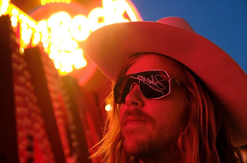 Der Schauspieler Lasse Sehsted Skafte als Cowboy, in dessen Sonnenbrille sich der Neonschriftzug mit Liberaces Signatur spiegelt – Bild: Kinescope Film Der Schauspieler Lasse Sehsted Skafte als Cowboy, in dessen Sonnenbrille sich der Neonschriftzug mit Liberaces Signatur spiegelt – Bild: Kinescope Film