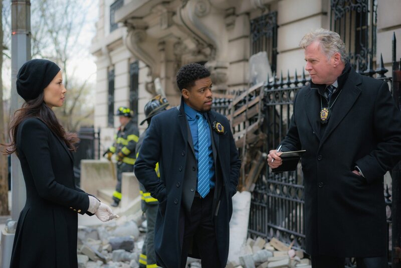 In Morlands Büro geht eine Bombe hoch. Watson (Lucy Liu, l.) und Holmes halten Moriartys Organisation für den Drahtzieher. Doch sie beschließen, das lieber vor Captain Gregson (Aidan Quinn, r.) und Detective Bell (Jon Michael Hill, M.) geheim zu halten und ermitteln auf eigene Faust … – Bild: Michael Parmelee