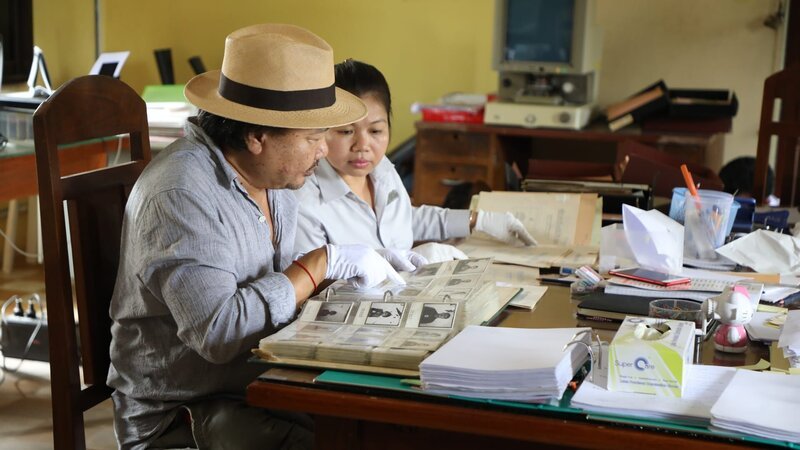Rithy Panh viewing photos of the prisoners of S-21 at the Tuol Sleng Genocide Museum Archive in Phnom Penh, Cambodia, with Sdan Somrithpisey. – Bild: Discovery Channel /​ Discovery Communications