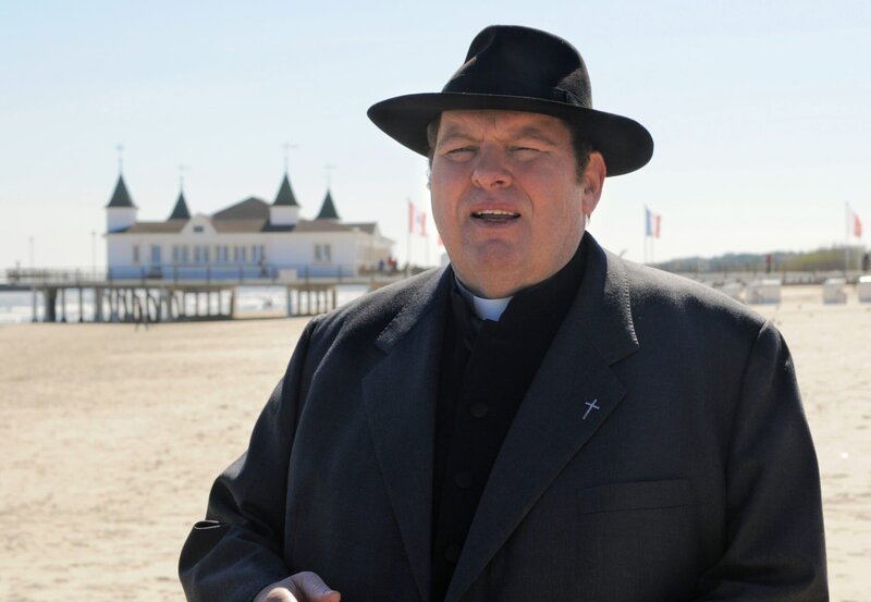 Pfarrer Braun (Ottfried Fischer) macht in seiner neuen Pfarrei auf Usedom einen Strandspaziergang. – Bild: ARD Degeto/​Reiner Bajo