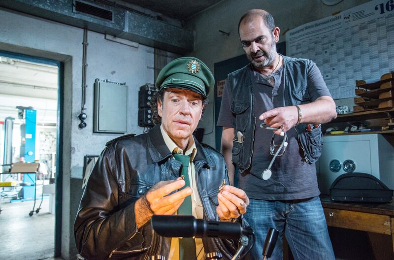Yazid (Hannes Ringlstetter, r.) erklärt Staller (Helmfried von Lüttichau, l.), wie die Maschine zum Schlüssel Nachmachen funktioniert. – Bild: ARD/​TMG/​Marco Meenen