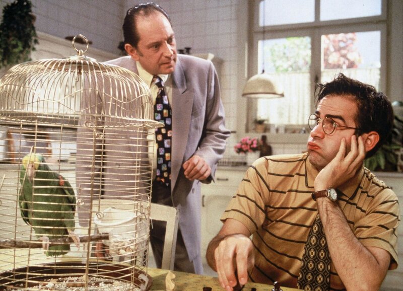 Bruno (Beat Marti) versucht sich verzweifelt auf das Schachspiel zu konzentrieren, doch das wird ihm von allen Seiten erschwert: Der Papagei will nicht still sitzen und Rolf (Andreas Matti) führt offensichtlich wieder etwas im Schilde. – Bild: SRF