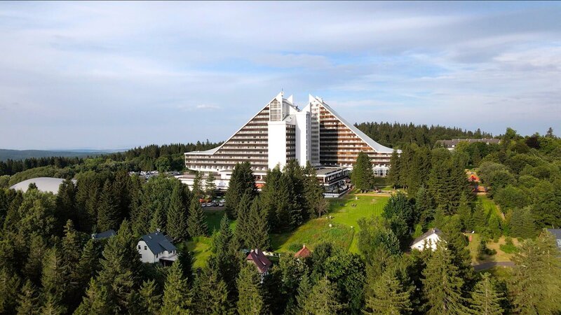 In der der DDR wurde gleich mit ihrer Gründung der Bau von Ferienkomplexen zur Pflicht, schrieb doch die Verfassung das Recht jeden Bürgers auf Urlaub fest. Das ehemals der Oberschicht vorbehaltene Privileg des Reisens durfte zu einem Volkssport werden. Dabei entstanden riesige Freizeitmaschinerien, die unter Verwendung moderner Baumaterialien eigene Architekturtypen generierten. So mischen sich in die Urlaubsarchitektur der ersten Jahrzehnte regional-nationale Traditionen mit sowjetisch-sozialistischem Klassizismus und der Klassischen Moderne. Mit der Ausweitung der Bauprogramme in den 60er Jahren erfolgte die Typisierung, die mit Modulen des allgemeinen Wohnungsbaus operierte. Dieser Linie folgend entstanden auf Rügen Urlaubssiedlungen, Visionen vom „sozialistischen Seebad“, die mit den Ferienzentren der großen europäischen Strände mithalten sollten. Für den Gebirgs- und Wintersporturlaub verwandelte man den thüringischen Gebirgsort Oberhof in ein neues „sozialistisches St. Moritz“. Hier entstanden repräsentative Interhotels und Ferienheime mit ehrgeiziger Architektur: So wurde die Bergtopographie durch abgetreppte und abgeschrägte Baukörper verlängert, die Ästhetik der Landschaft mit Bergspitzenmotiven und Dreiecksmotiven weitergeschrieben, unter Verwendung von vorwiegend Beton, aber auch regionalen Materialien wie Naturstein, Schiefer und Holz. Der Film „Urlaubsträume in Beton: DDR“ wirft einen prüfenden Blick zurück auf die architekturästhetische und soziologische „Haltbarkeit“ des damals Gebauten. – Bild: MDR/​ZAUBERBERGFILM
