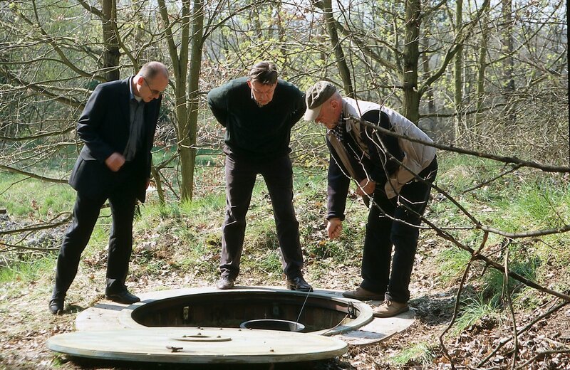 Hermann Thiele (Uwe Zerbe, r.) zeigt Dr. Robert Kolmaar (Ulrich Mühe, l.) und Kommissar Hoffer (Jörg Gudzuhn, M.) einen ehemaligen Brunnen, dessen Wasser mit Caesiumchlorid keimfrei gehalten wurde. – Bild: ZDF