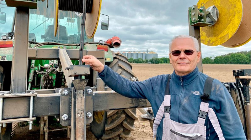 Landwirt Aton Hirl vor seinem selbst erfundenen Gerät mit dem er die Bewässerungsschläuche in den Acker bringt. – Bild: NDR/​Hanse TV