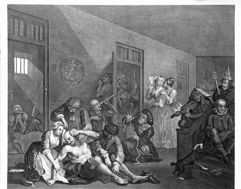 An insane man (Tom Rakewell) sits on the floor manically grasping at his head, his lover (Sarah Young) cries at the spectacle whilst two attendants attach chains to his legs; they are surrounded by other lunatics at Bethlem hospital, London. – Bild: Wellcome Library