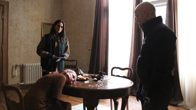 Petra Berger (Komparsein, M.) wird tot an ihrem Esstisch aufgefunden – gefesselt und geknebelt. Die Art und Weise wie die Leiche aufgefunden wurde, gleicht einem grausamen Stillleben. Mavi Neumann (Aybi Era, l.) und Robert Heffler (Jürgen Vogel, r.) rätseln über die Beweggründe des Täters. – Bild: ZDF