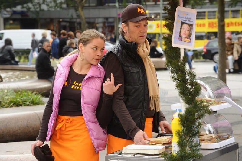 Katja (Karolina Lodyga, l.) begegnet Ken Wood zufällig wieder, als sie gerade mit Armin (Rainer Will, r.) Sandwiches verkauft. Sie versucht zwar aus Scham, ihre missliche Lage Ken gegenüber so gut es geht zu vertuschen, doch er durchschaut sie … – Bild: SAT.1 /​ Oliver Ziebe