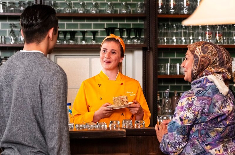 Als Sevim Sarah ein Stück Kuchen im Brunnerwirt vorbeibringt, fällt auf, dass Leon ihn nicht selbst gebacken, sondern gekauft hat. Von links: Leon (Joel Akgün), Sarah (Sophie Reiml), Sevim (Özay Aslanhan). Weiteres Bildmaterial finden Sie unter www.br-foto.de. – Bild: BR/​Lena Semmelroggen