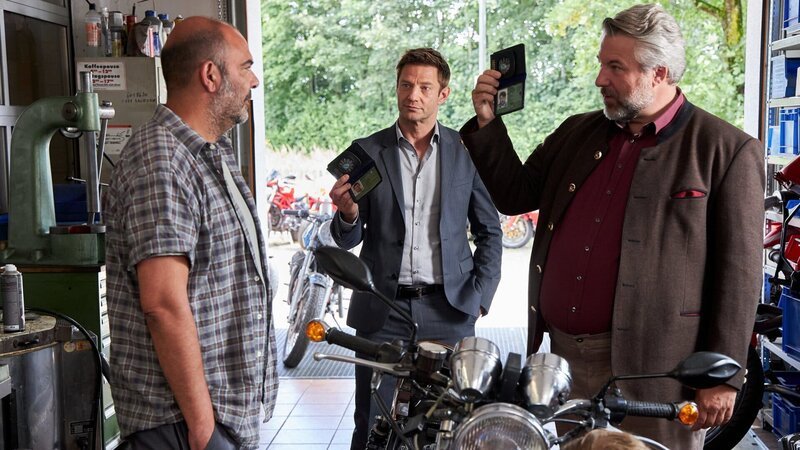 Die Kommissare Hansen (Igor Jefti?, M.) und Stadler (Dieter Fischer, r.) befragen den Besitzer einer Motorradwerkstatt, Bernhard „Bulli“ Kuhn (Hannes Ringlstetter, l.), denn das Mordopfer war sein Kunde. – Bild: ZDF