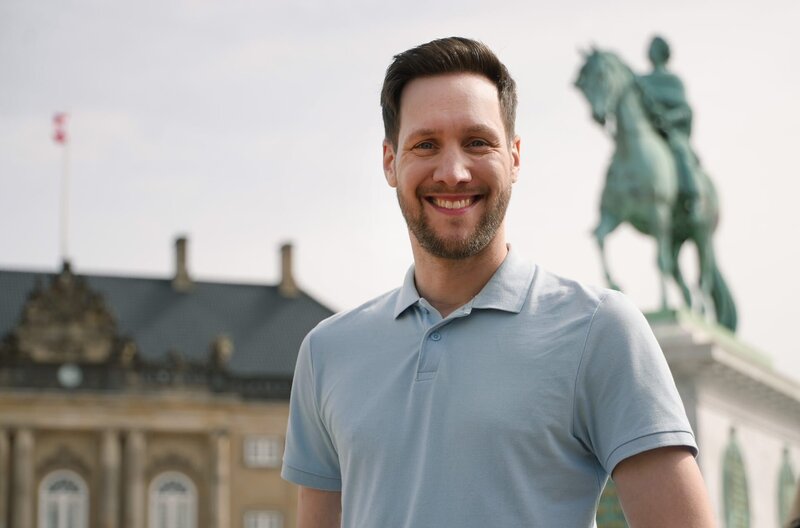 Reporter Sven Kroll vor Schloss Amalienborg. Seine fünftägige Reise in die dänische Hauptstadt darf 500 Euro kosten – Unterkunft, Verpflegung und Eintritte inklusive. Eine echte Herausforderung. – Bild: WDR/​SWR/​NDR/​Bavaria Entertainment GmbH