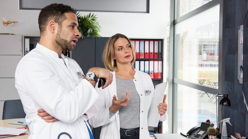 Die Oberäzte Dr. Matteo Moreau (Mike Adler, l.) und Dr. Franziska Ruhland (Gunda Ebert, r.) besprechen Samis komplizierte Bein-OP. – Bild: ARD/​Jens Ulrich Koch