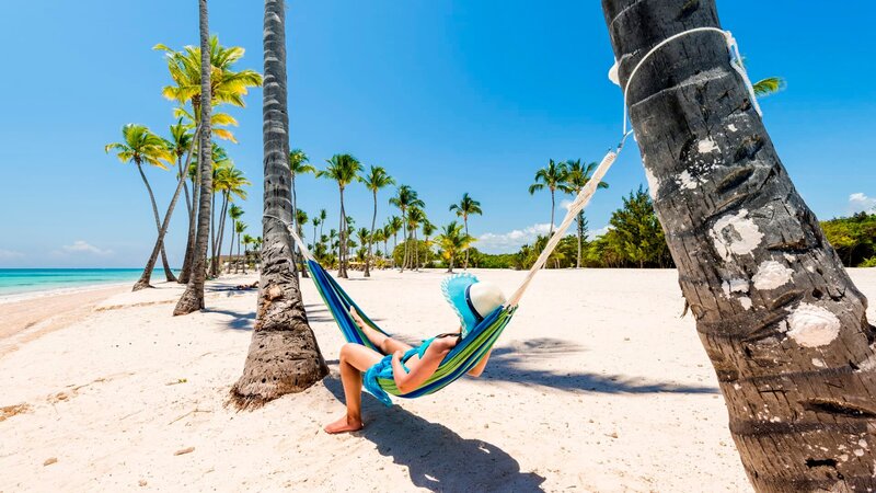 Juanillo Beach (playa Juanillo), Punta Cana, Dominican Republic. Woman relaxing on a hammock on a palm-fringed beach. – Bild: Marco Bottigelli /​ Getty Images /​ Moment RF