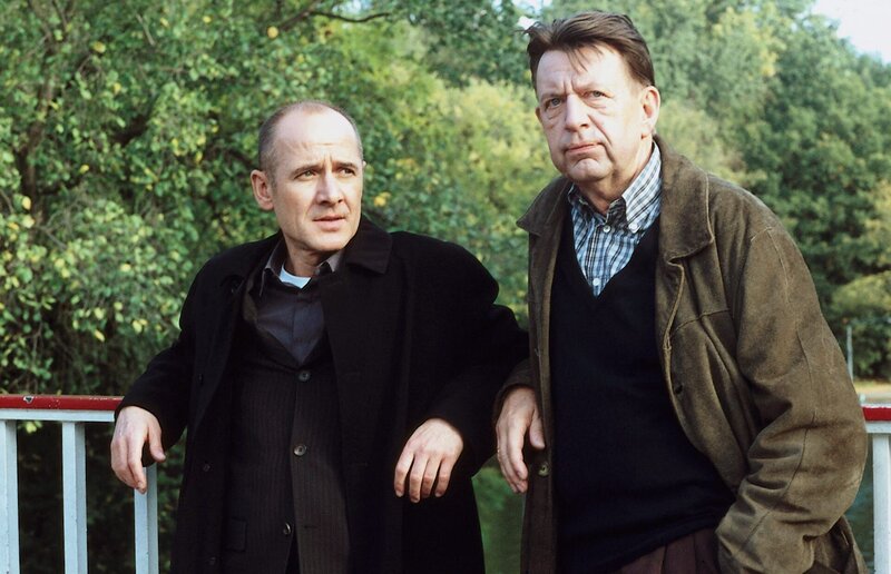 Dr. Robert Kolmaar (Ulrich Mühe, li.) und Kommissar Joe Hoffer (Jörg Gudzuhn, re.) vermuten, dass der Mord an Astrid Nichols aus gutem Grund inszeniert wirkte. – Bild: ZDF
