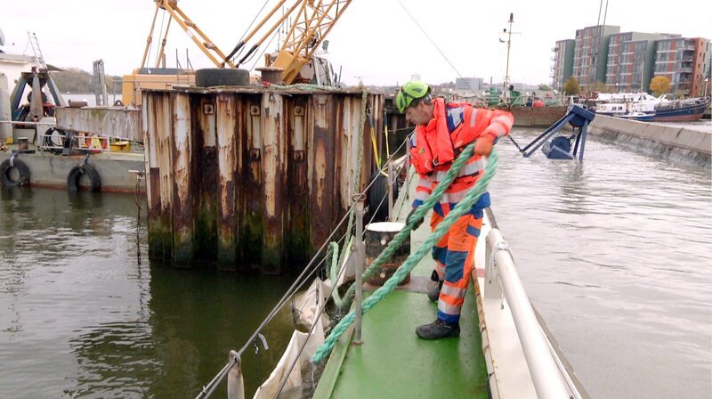 Anlegen der mit kontaminiertem Sediment gefüllten Schute HH 205 an der Schlickegrube Stadthafen Rostock – Bild: NDR Anlegen der mit kontaminiertem Sediment gefüllten Schute HH 205 an der Schlickegrube Stadthafen Rostock – Bild: NDR