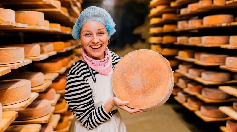 Marina präsentiert einen gereiften Käselaib. – Bild: BR/​megaherz gmbh/​Hans-Florian Hopfner
