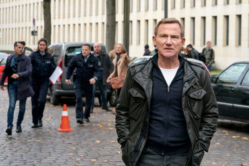 Overbeck (Roland Jankowsky) ist im Einsatz, um einen Autounfall mit Todesfolge zu untersuchen. Die Stimmung unter den Besitzern der beschädigten Autos ist gereizt. – Bild: ZDF/​Thomas Kost