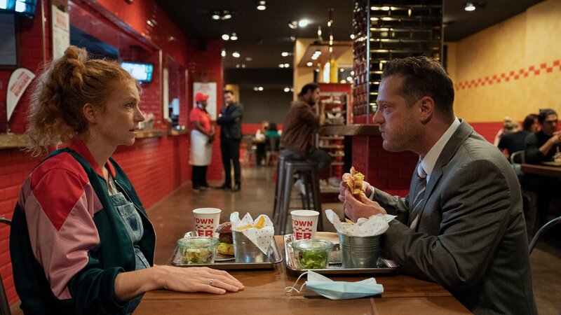Mabel Kruse (Marleen Lohse, l.) sitzt nach dem Bewerbungsgespräch ihres Mannes Kevin Kruse (Aurel Manthei, r.) mit ihm im Burgerladen. Im Hintergrund steht der Filialleiter Mübariz Pettekaya (Kais Setti, 3.v.l.) und wartet auf die Polizei. – Bild: 3sat