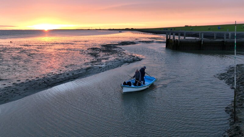 Früh morgens bei Niedrigwasser gelangen die Gebrüder Hellmann nur mit dem kleinen Beiboot zu ihrem Passagierschiff, mit dem sie Exkursionen ins Watt unternehmen. – Bild: NDR/​Ralf Biehler/​Johannes Rudolph