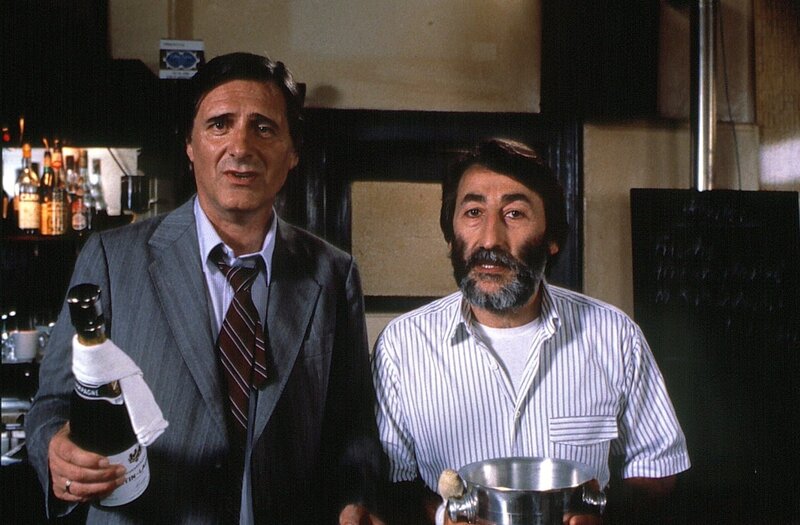 Josef Haslbeck (Helmut Fischer, links) preist sich mit Erfolg Giancarlo (Aurelio Ferrara) an – nur so kann er wieder einmal dem drohenden Rausschmiß von Ilse entgehen. – Bild: Bayerischer Rundfunk