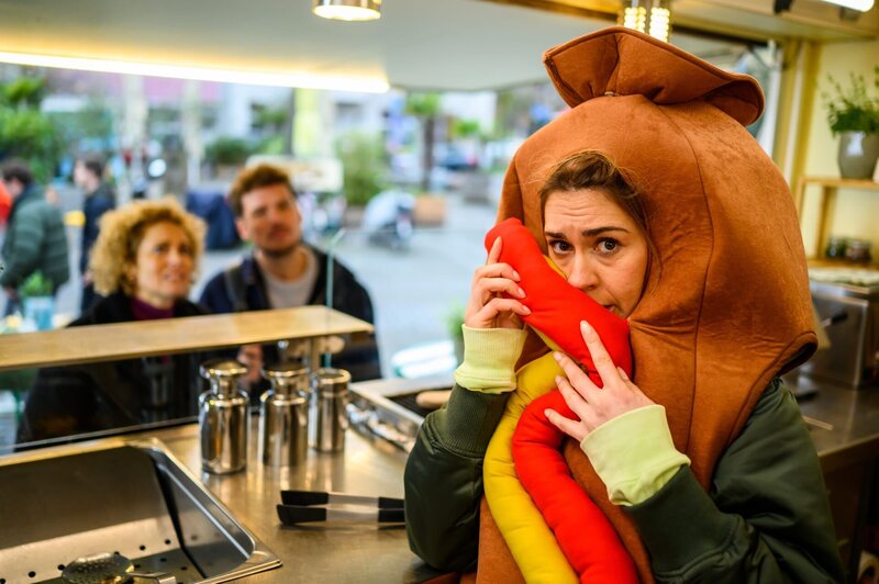 Betty Hertz (Henrike Hahn) versucht unerkannt zu bleiben, als Dr. Julius Walden (Constantin Lücke, M.) und Dr. Helena von Arnstett (Claudia Hiersche, l.), unerwartet bei ihr an der Würstchenbude auftauchen. – Bild: ZDF und Julia Feldhagen
