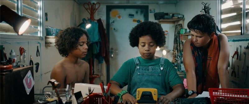 Felix (Junes Callaert, links) und Sammy (Arthur Hermans, rechts) bitten Noor (Maja Azila) um Hilfe, die versucht, den Walkman zu reparieren. – Bild: VRT/​Nico Surings