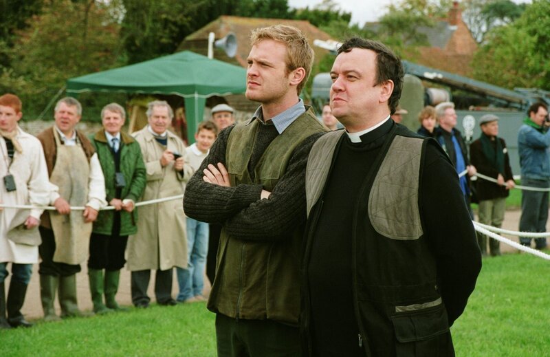 Reverend Anthony Gant (Richard McCabe) muss sich zu Pferd gegen eine Schar Frauen behaupten – so will es die Tradition dieses Dorffestes. Roland Marwood (Joseph Kennedy) wird ihm die Daumen drücken. – Bild: port.hu