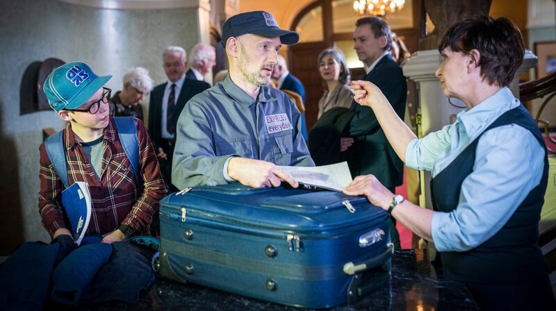 Benny (Ruben Storck, links) recherchiert im Auktionshaus und beobachtet, wie ein Lieferant (Timo Werner) einen mysteriösen Koffer bei der Garderobiere (Annette Bajorat) abliefert. – Bild: NDR/​Boris Laewen
