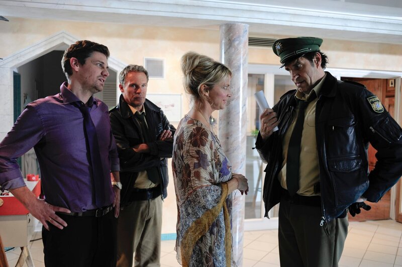 Hubert (Christian Tramitz, 2.v.l.) und Staller (Helmfried von Lüttichau, r.) konfrontieren Andrea Manninger (Ursula Gottwald) mit dem Bild, auf dem der tote Fabian Pfeifer nackt in ihrem Garten zu sehen ist. – Bild: Leonine /​ Chris Hirschhäuser