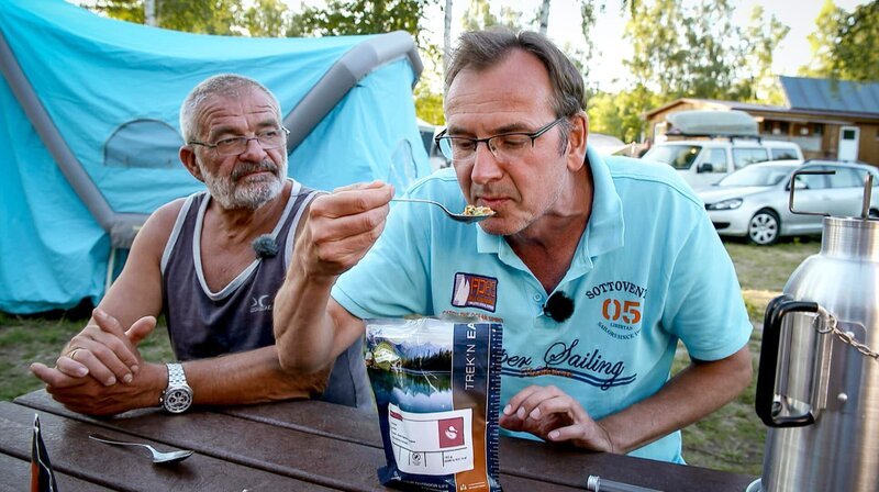 Stefan Peine (re.) und Bernd Kuhn auf dem Campingplatz Bergwitzsee, Stefan testet Campingessen. – Bild: MDR/​timeline